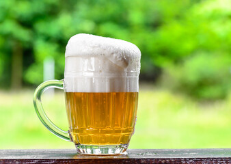 Golden refreshing beer with thick foam against the background of a green lawn,