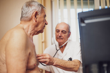 Obraz premium Patient is having exam at pulmonologist. Doctor is listening heart beats and lungs sound of his patient.