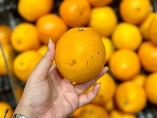 Women's hand picking fresh oranges stacked in a supermarket – vibrant, juicy, and packed with vitamin C for a healthy boost, Alam Sutera, Indonesia - March 16, 2025.