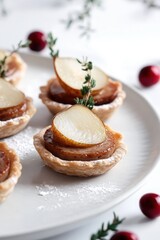 Beautifully detailed photograph of festive mini tartlets with golden brown flaky crust, filled with creamy duck pate and topped with delicate pickled pear slices, presented on a clean white plate