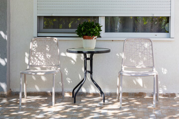  Cozy patio seating with table and potted plant in dappled sunlight near window for outdoor lifestyle concept