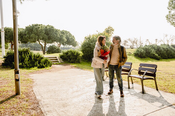 Couple, man standing and looking at woman walking next to him and holding a plant, they are smiling, outdoors, on a sunny day