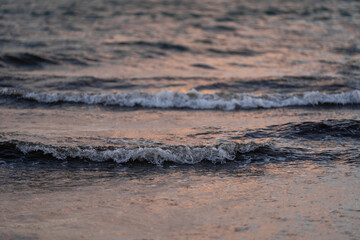 Close-up of gentle waves rolling across the surface of the sea at dusk. The soft lighting reflects off the water, creating peaceful and serene atmosphere