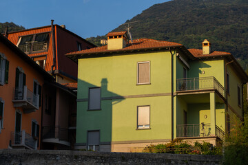 Brightly colored houses with balconies in small mountain village, bathed in warm sunset light. Green and orange facades contrast with the natural backdrop