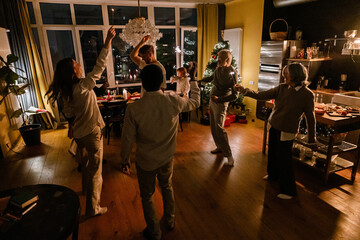 Obraz premium Family and guests stand in a circle and dance while holding lit sparklers in the living room near the kitchen during Christmas