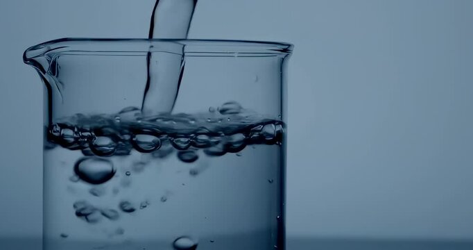 Anamorphic video of glass beaker filled with water, surrounded by bubbles on a light blue background 