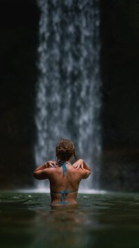 Portrait: young girl posing at a waterfall posing. Beautiful woman stands in the water of a river on island Bali, Indonesia. Sexy female has wet hair. Travel tourism, vacation concept. wild nature
