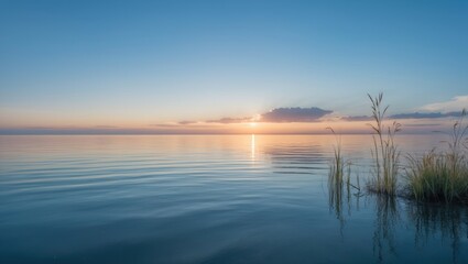 Obraz premium Sea at sunset with a clear blue sky creating a natural mirror reflection on the water and golden grey clouds on the horizon during dusk.