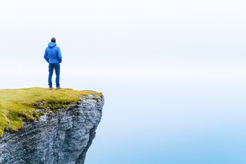 Obraz premium Solitary person standing on a cliff edge, gazing into the misty horizon, symbolizing contemplation, freedom, and vast possibilities. 