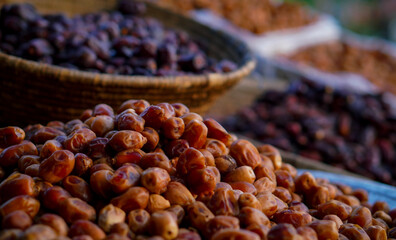 A pile of golden-brown dates in focus with baskets of darker dates in the background at an outdoor market.