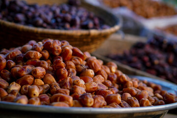 A close-up of golden-brown dates piled in a metal tray with darker dates in woven baskets in the background at an outdoor market.