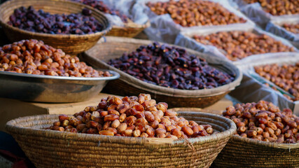 Various types of dates displayed in woven baskets and metal trays at an outdoor market, showcasing different shades and textures.