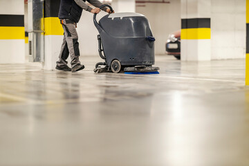 An unrecognizable washer man cleaning garage floor with washing machine.