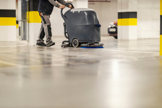 An unrecognizable washer man cleaning garage floor with washing machine.