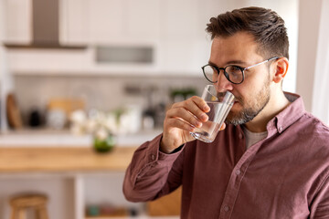 A thoughtful man takes a break, drinking a glass of water in a home kitchen. He values wellness, focus, and self-care, ensuring hydration is part of his daily lifestyle and healthy habits.