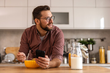 A man in a casual outfit enjoys his breakfast while working on his laptop in a modern kitchen. He starts his day with a nutritious meal, focusing on productivity and well-being.