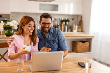 A happy couple working together on a laptop while reviewing documents. They share a moment of...