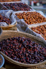 A close-up of dark, shiny dates piled in a woven basket with more varieties in the background at a market.