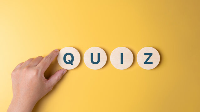 Hand places wooden circles with word QUIZ on a yellow background, symbolizing the start of an engaging and fun quiz activity. Invites participants to test their knowledge and enjoy the challenge.