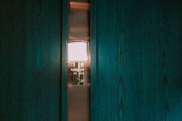 Illuminated wall sconce casting soft glow on dark teal wood paneling