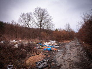 An illegal landfill along a damaged forest road with piles of construction waste, plastic waste and other trash polluting the natural landscape.