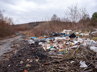 An illegal landfill along a damaged forest road with piles of construction waste, plastic waste and other trash polluting the natural landscape.