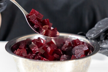 freshly chopped beetroot in a spoon over a metal bowl, preparing ingredients for homemade vinaigrette or other salads, chef wearing black gloves