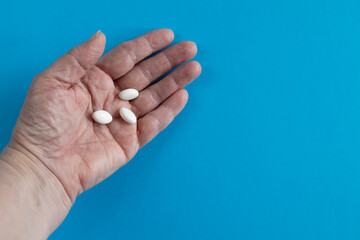 White pills in a hand on a blue background.