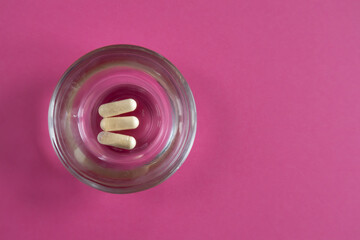 Capsules in a glass container on pink background.