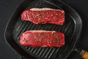 Juicy steaks seasoned with spices ready for grilling on a cast iron skillet