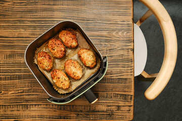 Roasted meat patties in an air fryer basket, resting on a wooden table