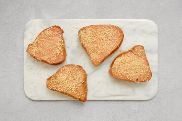 Four tuna steaks topped with sesame seeds on a marble serving board