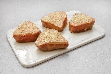 Tuna steaks coated with sesame seeds on a marble cutting board in a kitchen setting
