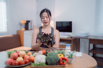 Young woman in sportswear holding fresh red oak lettuce while preparing a healthy meal with organic vegetables in a home kitchen, promoting clean eating and balanced nutrition