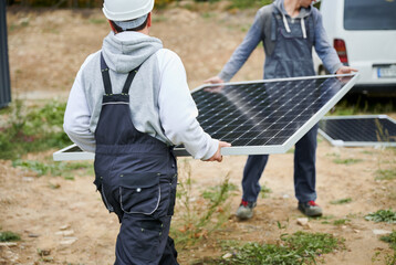 Installers installing solar panel system. Men workers in helmets carrying photovoltaic solar module...