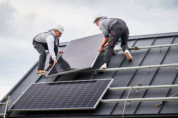 Installers installing solar panel system on roof of house. Men workers in helmets carrying...