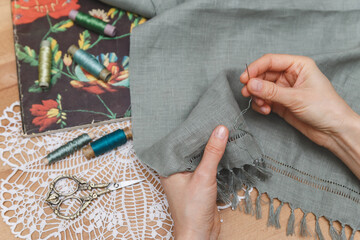 Hands meticulously working on openwork embroidery on grey fabric, surrounded by vintage scissors,...