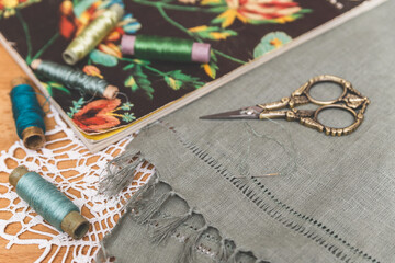 Green fabric with openwork embroidery, vintage scissors, thread spools, and floral book on a lace doily. Perfect for crafting, textile art, or vintage decor themes.