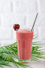 Strawberry cocktail, smoothie from strawberries, coconut cream, green buckwheat with straws in glass with palm leaves on a table. Lactose and sugar free. Vertical orientation.