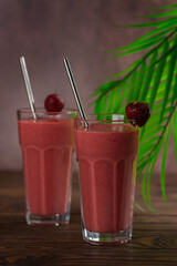 Glasses of strawberry milkshake, smoothie with palm leaves on brown background. Healthy drink. Lactose and sugar free. Vertical orientation.