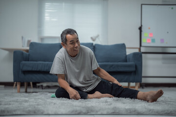Fototapeta premium Asian elderly man engaging in physical therapy and stretching exercises on the floor of his home, enhancing health and flexibility while enjoying an active lifestyle in retirement