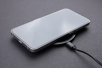 Mobile smartphone on wireless charging device on dark background.