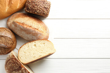 Whole and cut bread loafs on white wooden table, flat lay. Space for text