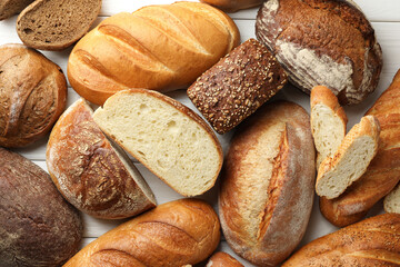 Whole and cut bread loafs on white wooden table, flat lay