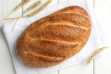 Loaf of bread with sesame seeds and spikes on white wooden table, flat lay