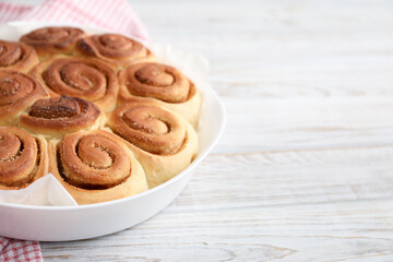 Freshly baked cinnamon rolls on light wooden table, closeup. Space for text