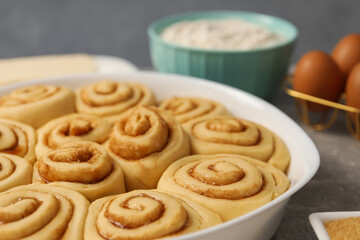 Raw cinnamon rolls in baking dish on table, closeup
