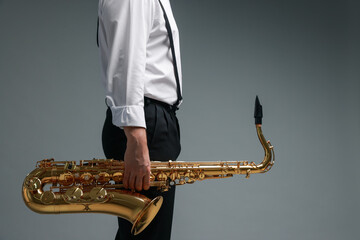 Professional musician with saxophone on grey background, closeup