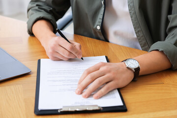 Client signing notarial document at wooden table in office, closeup