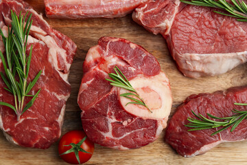 Pieces of raw beef, rosemary and tomato on wooden table, flat lay